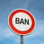 Traffic sign reads BAN against blue sky.