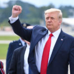 Donald Trump raising their arm in a fist gesture near a car.
