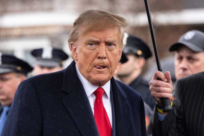 shutterstock_2442962269.jpg featured image Donad Trump stands under an umbrella.