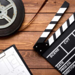 Film reel, clapperboard, and storyboard on wooden table.