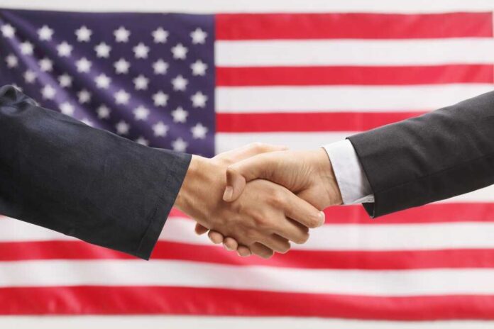shutterstock_2454737145.jpg featured image Two hands shaking in front of American flag