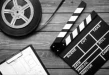 Film reel, storyboard, and clapperboard on wooden surface.