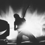 Silhouetted guitarist performing on stage with dramatic lighting.