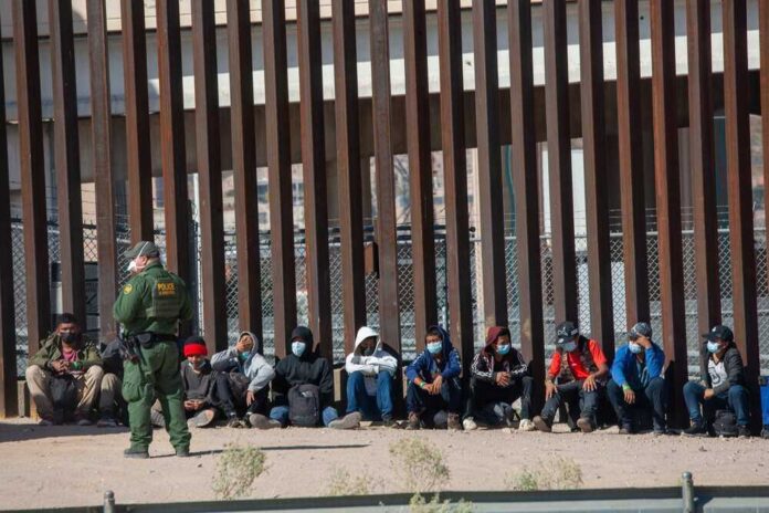 shutterstock_2079408463.jpg featured image Border patrol officer watches group sitting by a fence.