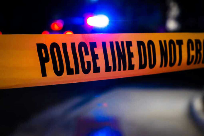 2408118125 Police tape with flashing lights in the background.