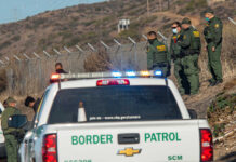 Border Patrol officers detaining individuals near a fence.