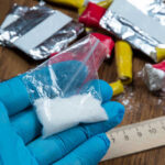 Blue-gloved hand holding bag of white powder