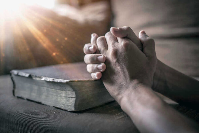 Hands praying over a Bible with sunlight