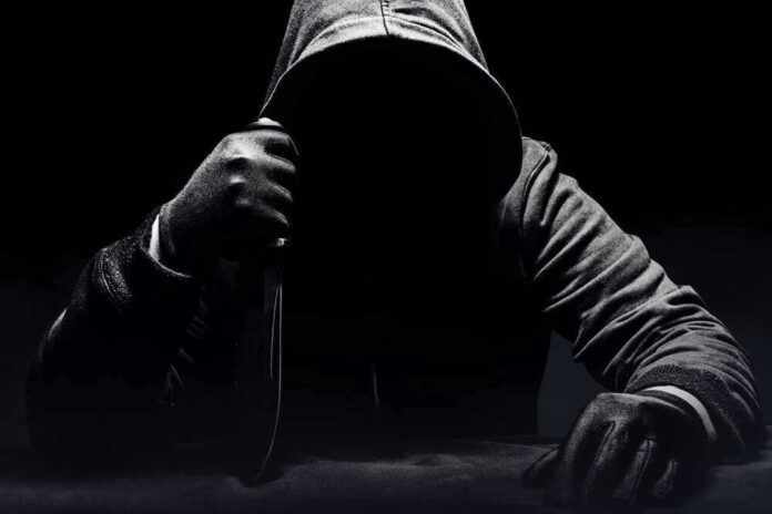 Person in dark hoodie holding a knife ominously