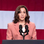 Kamala’s $1.5 BILLION Disaster A woman speaks at a podium with microphones.