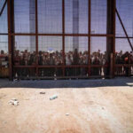 People standing behind a fence on a dusty path