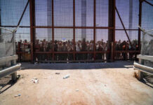 People standing behind a fence on a dusty path