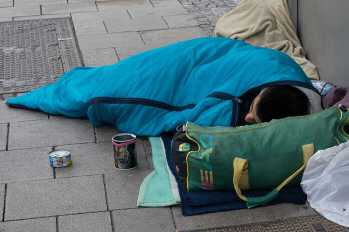 Person sleeping on pavement in a blue sleeping bag
