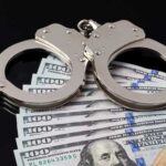 Federal Cop LOOTS $330K From Helpless Seniors Handcuffs resting on a stack of hundred dollar bills
