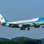Airplane flying above trees with blue sky background