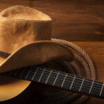Cowboy hat on guitar next to coiled rope.