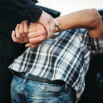 249 Arrests — Bar Chaos Explodes Again Person in handcuffs arrested by police officer.