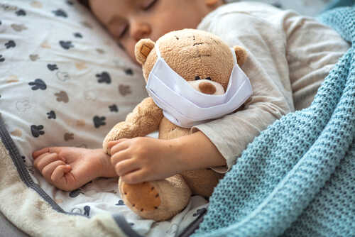 A sleeping child holding a teddy bear wearing a mask