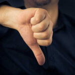 Hand showing thumbs down gesture, dark background.