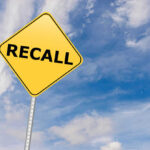 Yellow sign with RECALL text against blue sky.