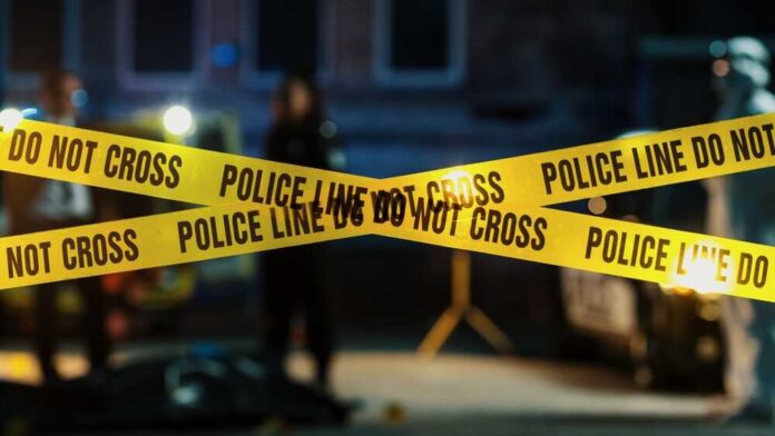 shutterstock_2230640037.jpg Police tape marking a crime scene with blurred figures in the background