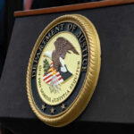 DOJ HUMILIATED Twice – She Walks Free Again Department of Justice seal on a podium.