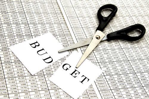 Scissors cutting a paper labeled 'BUDGET' on a financial spreadsheet