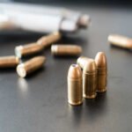 Mass Shooting: 12 Dead, Including Children Close-up of bullets on a dark surface with a handgun in the background