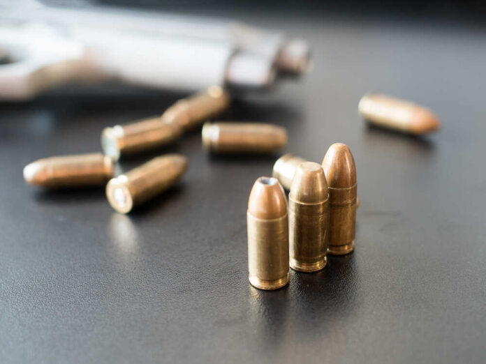 Close-up of bullets on a dark surface with a handgun in the background