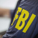 SHOCKING Confession Rocks FBI Person wearing FBI jacket, letters in yellow.