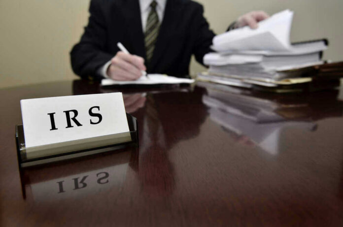 shutterstock_158874281.jpg IRS sign on desk, person handling paperwork behind.