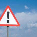 Deadly Inmate Riot ROCKS Prison Triangle warning sign with exclamation mark against sky.