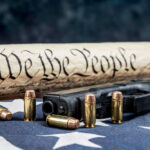 MASSIVE Gun Rights Victory Coming — Blue States Panic Gun, bullets, Constitution scroll on American flag.
