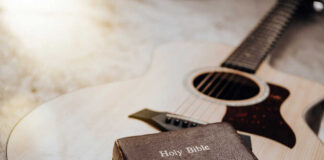 An acoustic guitar next to a Holy Bible on a soft surface