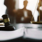 Gavel and scales in courtroom with blurred figures behind.