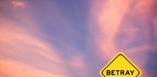 A yellow warning sign with the word 'BETRAY' against a colorful sunset sky
