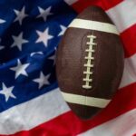 Power Struggle FREEZES College Football An American football resting on a background of the American flag