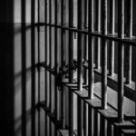 CIA Traitor Dies Behind Bars Rusty prison cell bars in dim lighting.
