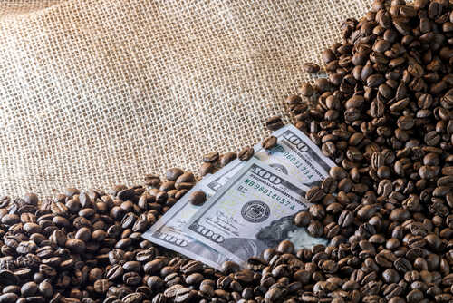A hundred dollar bill partially buried in coffee beans on a burlap background