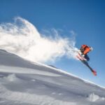 Skier jumping off a snow-covered slope against a clear blue sky