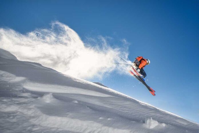 Skier jumping off a snow-covered slope against a clear blue sky