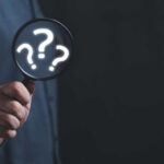 TERRIFYING Clues Spark Search For TV Host’s Mom Hand holding magnifying glass with question marks.