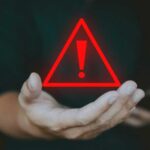 Trump Bank Crackdown Sparks Privacy Panic A hand holding a red warning triangle with an exclamation mark