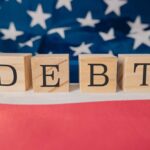 WARNING: America’s Ticking Debt Time Bomb Wooden blocks spelling 'DEBT' on a background of the American flag