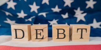 Wooden blocks spelling 'DEBT' on a background of the American flag