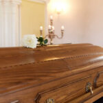 TV Icon Dead At 48 A wooden casket with a white rose placed on top in a solemn setting