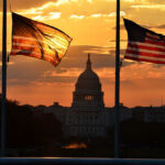 Silhouetted American flags in front of the Capitol building during sunset