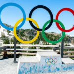 Olympic rings and podium with mountain backdrop.
