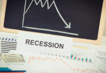 A sign reading 'RECESSION' in front of various financial charts and a downward trend graph