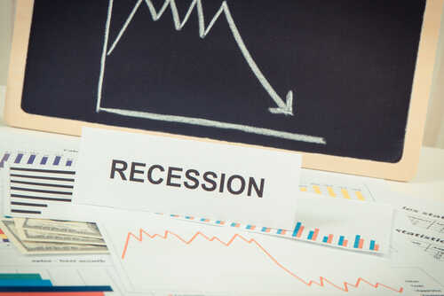 A sign reading 'RECESSION' in front of various financial charts and a downward trend graph